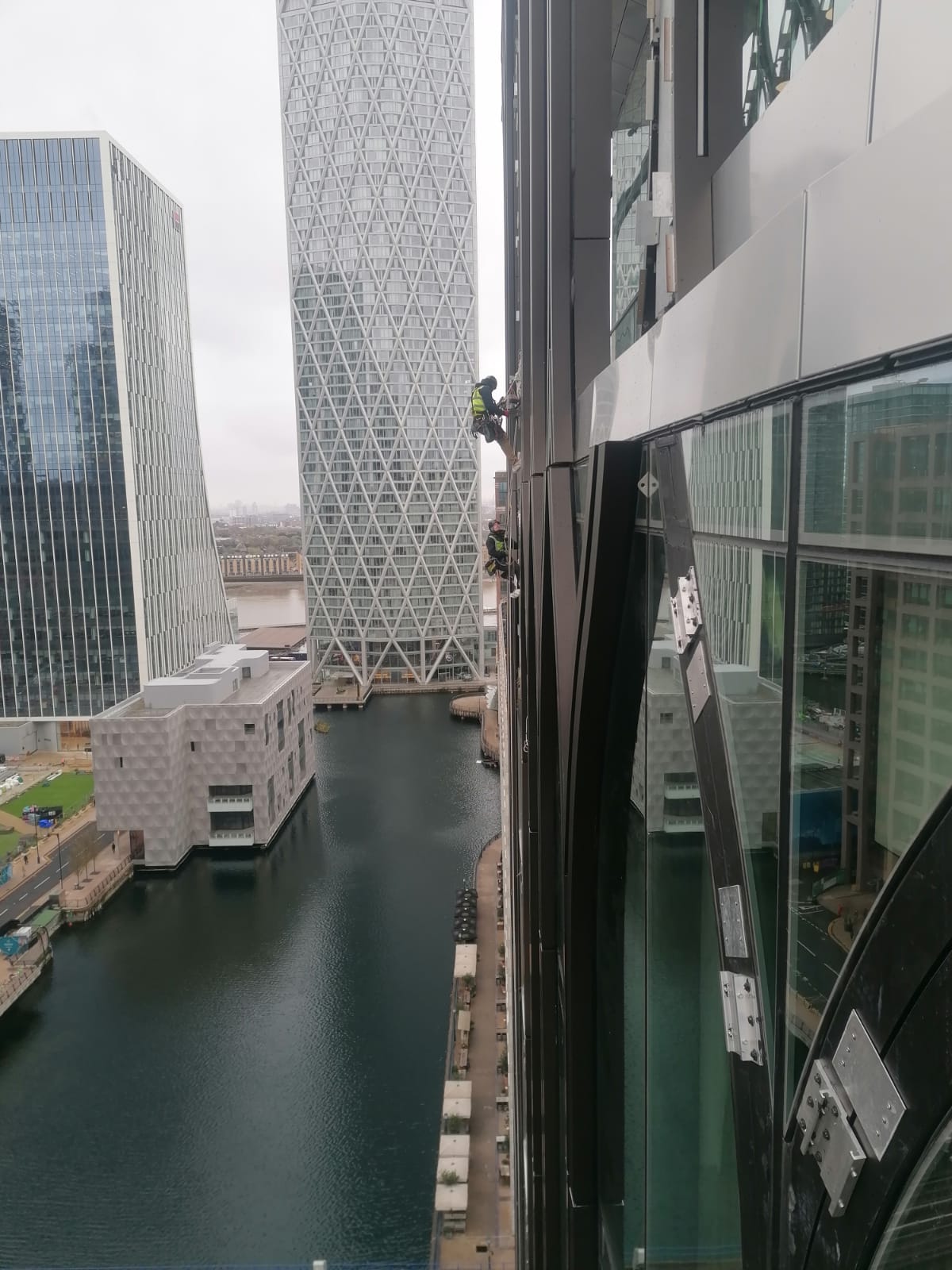Rope access inspection and maintenance works conducted on a glass façade within a dense urban environment.